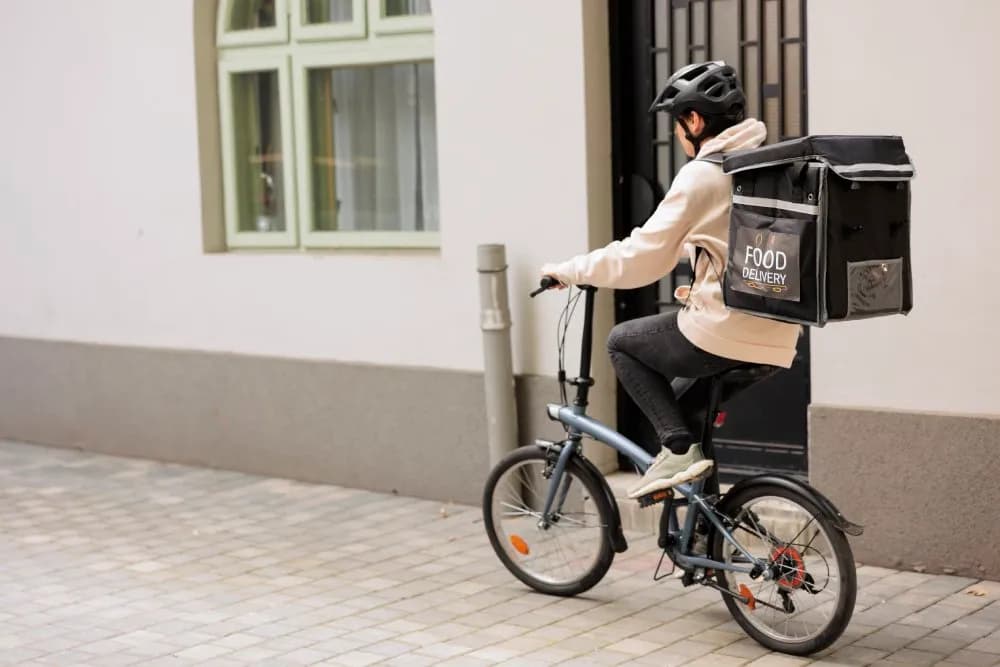 A delivery courier takes a video call on a phone while sitting on an e-bike outside.